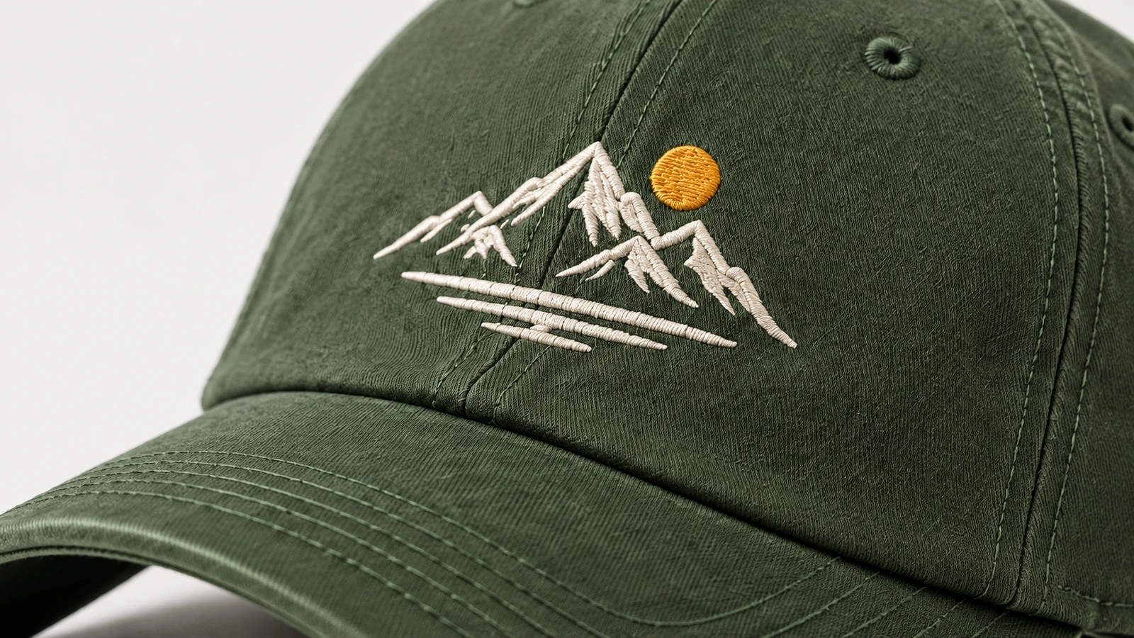 Close-up bordir gunung putih dan matahari kuning pada topi hijau