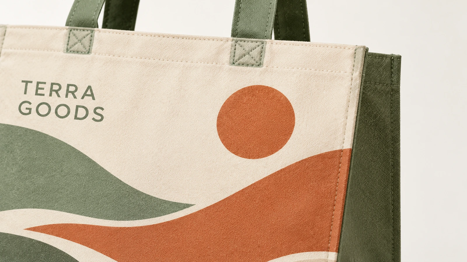 Permukaan tote tercetak dan jahitan pegangan Close-up tote cetak lanskap dengan tulisan TERRA GOODS dan pegangan hijau yang dijahit